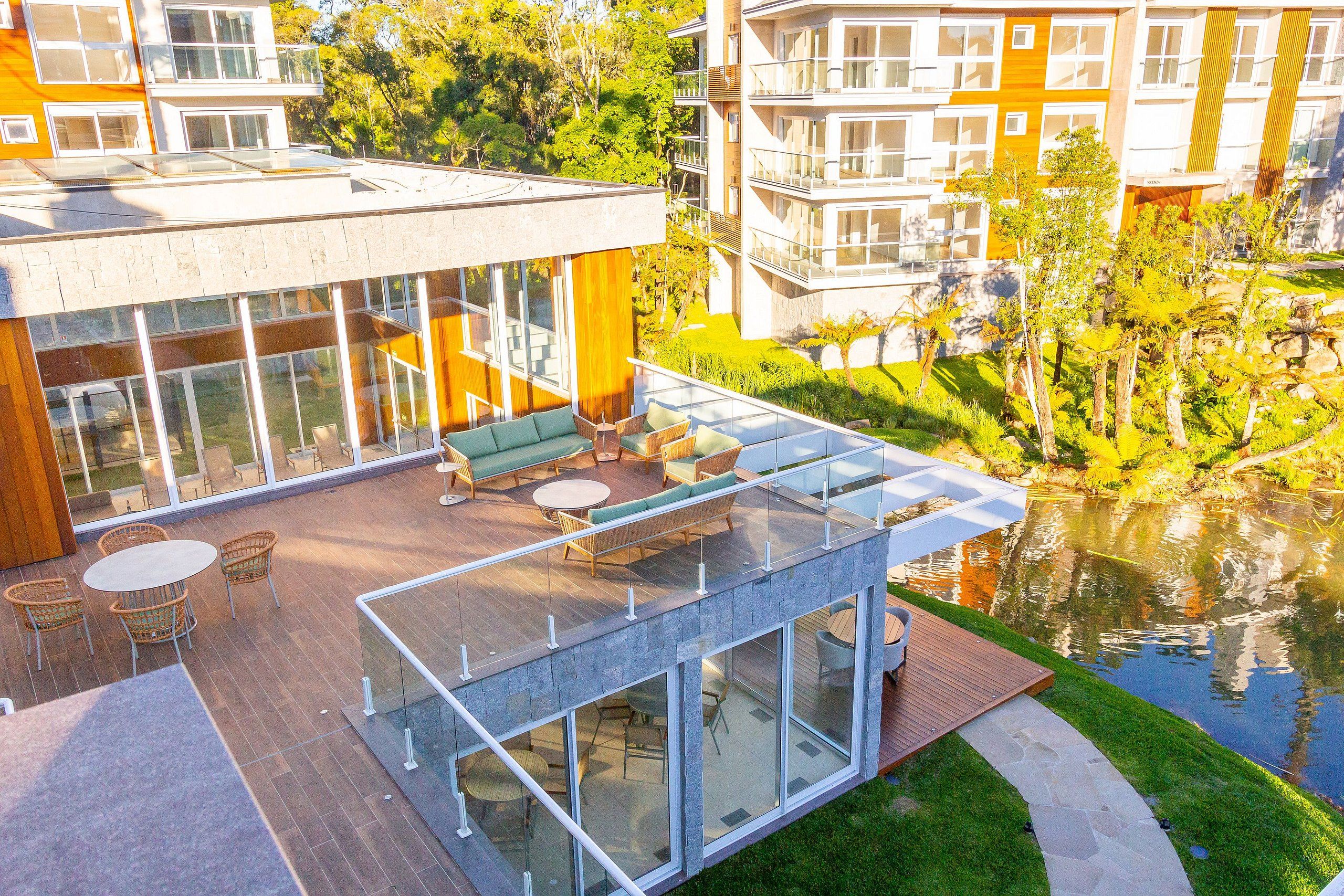 Un bâtiment moderne doté d’une véranda en verre, d’un espace extérieur aménagé pour s’asseoir et d’un bassin.