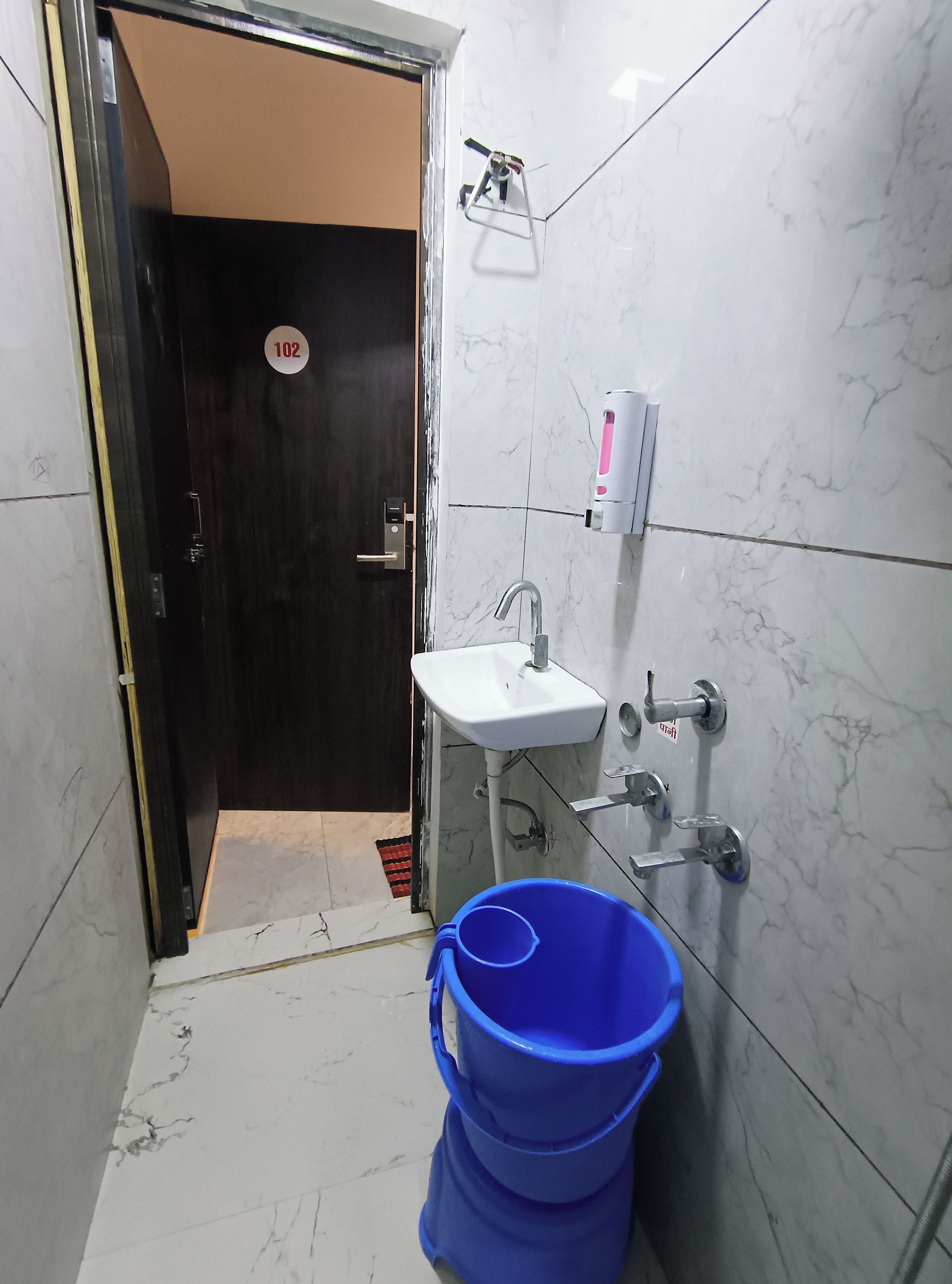 A small bathroom with a sink, a soap dispenser, and a blue bucket.