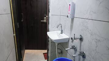 A small bathroom with a sink, a soap dispenser, and a blue bucket.