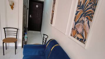 Ein Wohnzimmer mit einem blauen Sofa, einem Sessel, einem kleinen Tisch und einer Tür im Hintergrund.