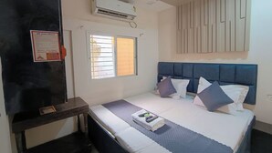 Quarto de hotel com cama, escrivaninha, janela com grades, ar condicionado e ventilador de teto.
