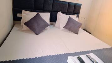 Ein Bett mit dunklem Kopfteil, zwei Kissen, einer Decke und zwei Fernbedienungen auf einem Handtuch.