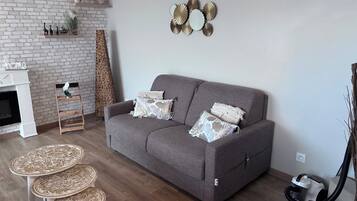 Un salon avec un canapé gris, deux coussins décoratifs, une cheminée blanche, un mur en briques et un élément décoratif fixé au mur.
