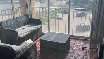 Un balcon doté de meubles en osier et offrant une vue sur la mer et les bâtiments.