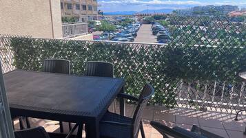 Un balcon avec une table et des chaises, donnant sur un parking et des immeubles.