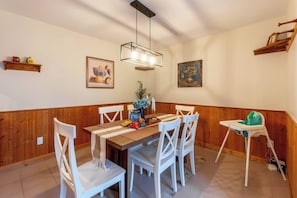 A dining area with a wooden table, white chairs, a baby high chair, and wall-mounted shelves with decorative items. - Urban cabin near chocolate lake with sauna (Halifax)