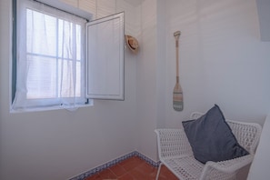 Ein Zimmer mit einem weißen Korbstuhl, einem Fenster mit weißem Vorhang und einem Schläger an der Wand.