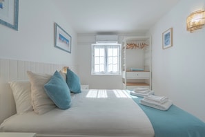 Ein Schlafzimmer mit Bett, Kissen, einem Fenster, einer Klimaanlage, einem Kleiderschrank und einer Pendelleuchte.
