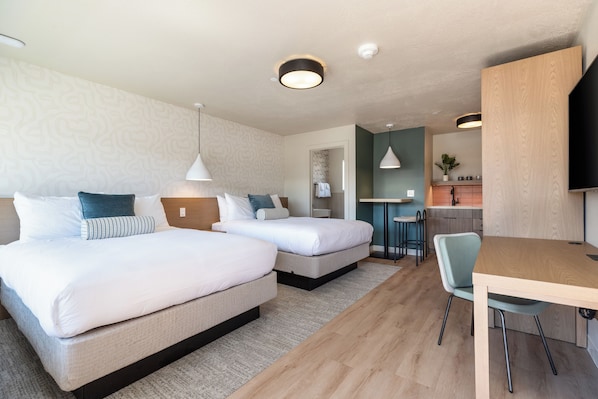Une chambre d’hôtel avec deux lits, un bureau, une chaise, une télévision et une kitchenette.