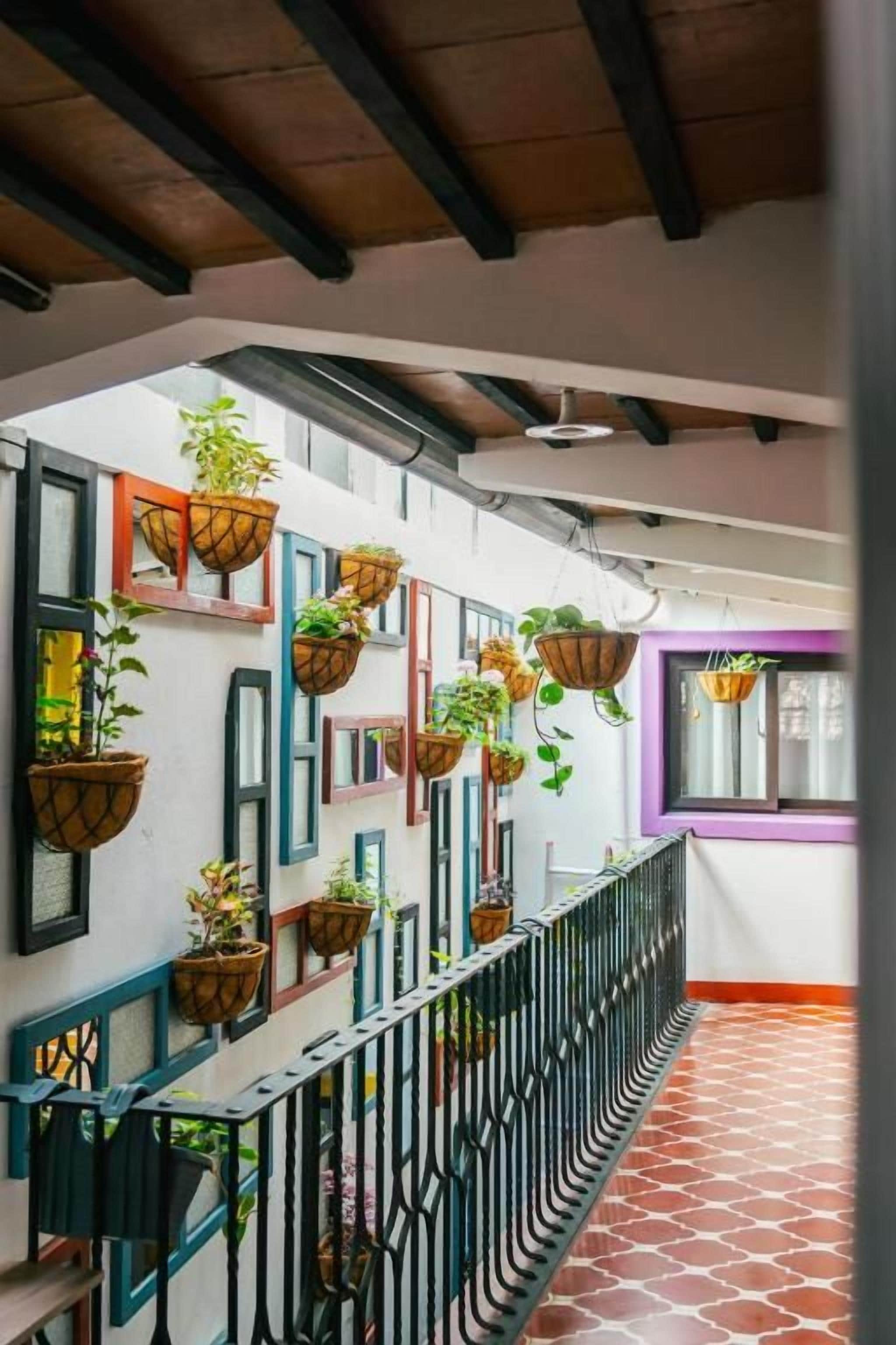 A corridor with a tiled floor, a black metal railing, and hanging planters with plants.