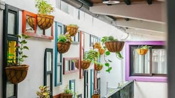 A corridor with a tiled floor, a black metal railing, and hanging planters with plants.