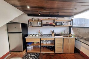 Cuina compacta amb nevera, fogó, forn de microones i armaris de fusta.