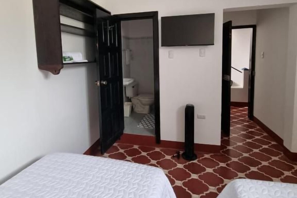 Habitació amb dos llits, un armari, televisió i un bany visible a través d'una porta oberta.