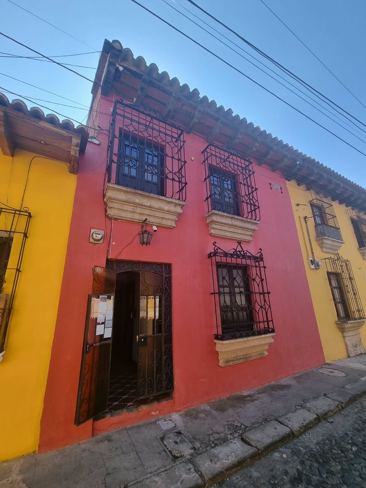 Un edificio con fachada roja, rejas negras en las ventanas y un edificio amarillo contiguo.