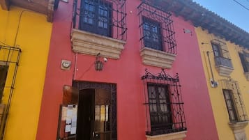 Un edificio con fachada roja, rejas negras en las ventanas y un edificio amarillo contiguo.