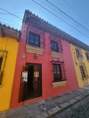 A building with a red facade, black window bars, and a yellow adjacent building. - Casa Capirucho (Antigua Guatemala)