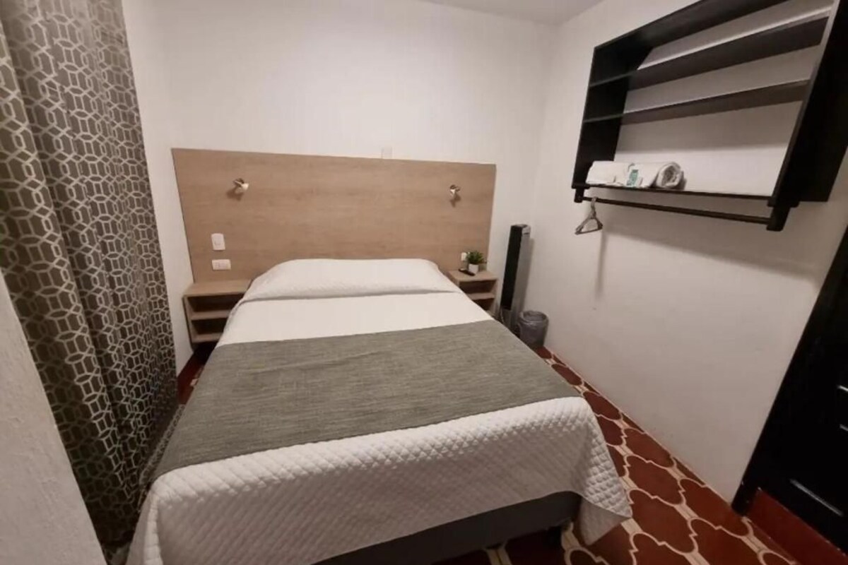 Habitació d'hotel amb llit, una taula de nit, prestatge fixat a la paret i un terra amb disseny.