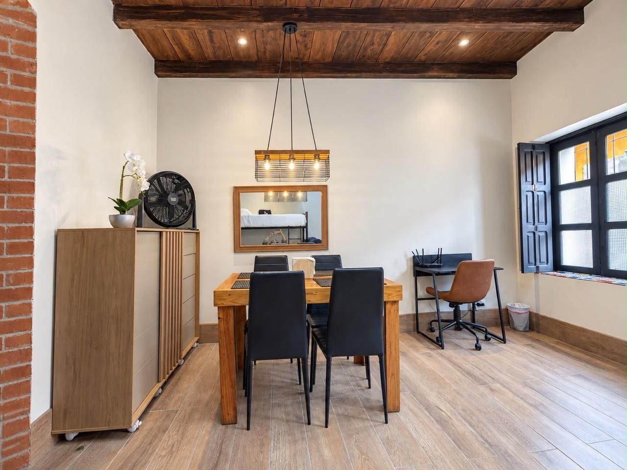 A dining area with a wooden table, black chairs, a wooden cabinet, and a ceiling fan.