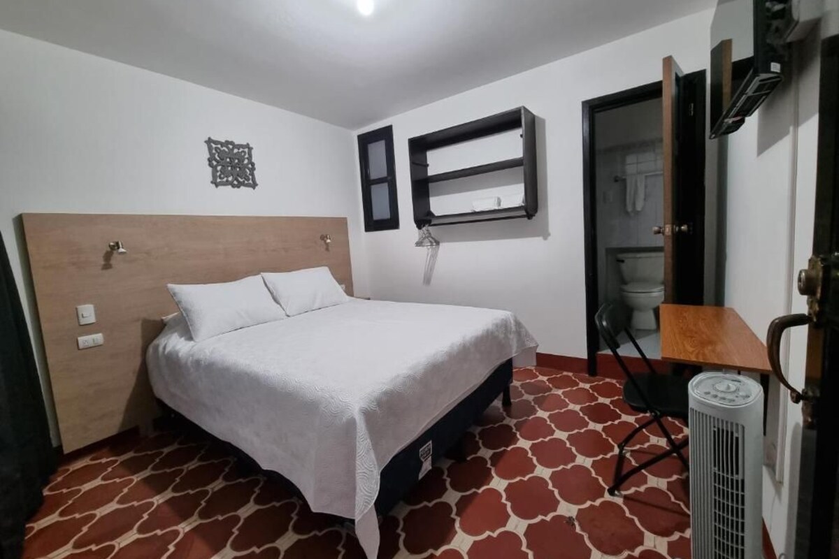 Habitación de hotel con cama, escritorio, silla, radiador y ventana.