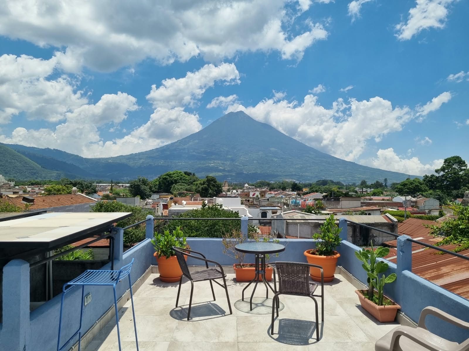 Una terraza en la azotea con mobiliario exterior, plantas en macetas y vistas a la montaña.