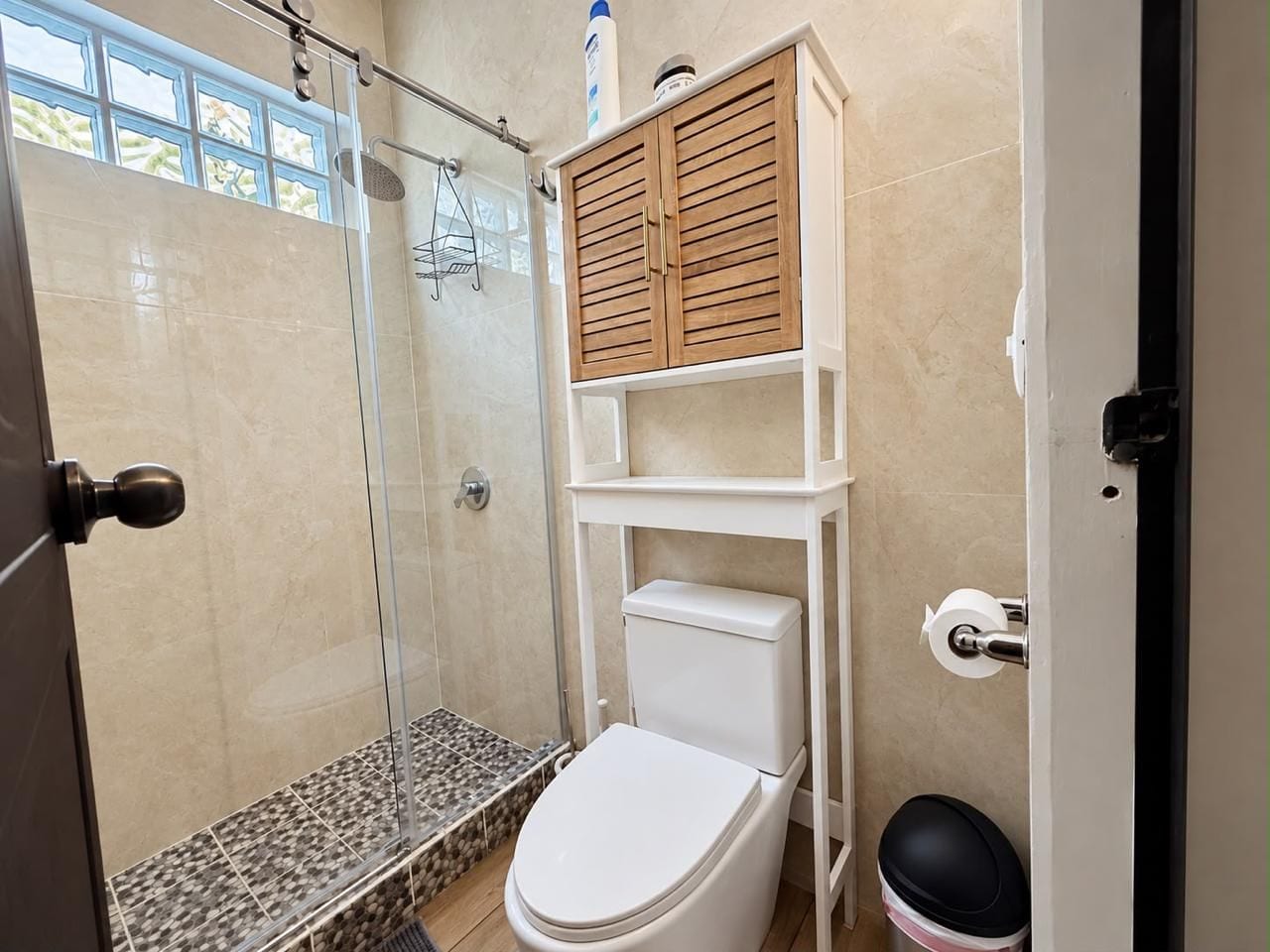 A bathroom with a glass-enclosed shower, a toilet, and a wooden cabinet above the sink.