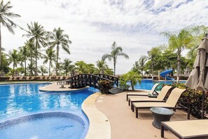Ein Poolbereich mit Liegestühlen, einer Brücke und Palmen.
