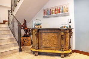 Eine Treppe mit Holzwand, eine dekorative Skulptur eines Pferdes, ein Holzkabinett mit aufwendigen Schnitzereien und ein an der Wand befestigtes Gemälde von farbenfrohen Flaschen.