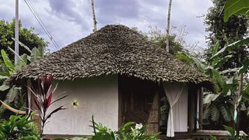 A small, single-story structure with a thatched roof, surrounded by lush greenery.