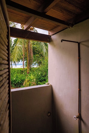 A shower area with a view of a tropical landscape, including palm trees and a body of water. - Luzul Ecohotel (Arusi)