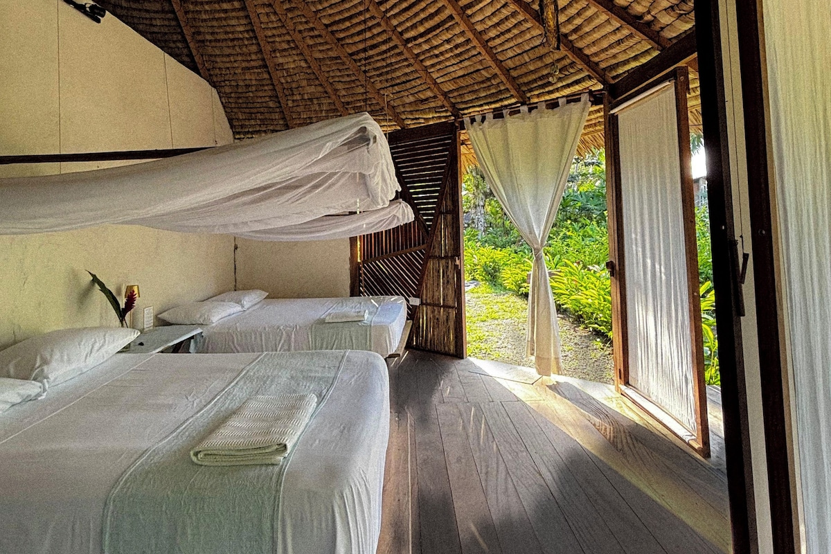 A room with two beds, a wooden floor, and a thatched roof.