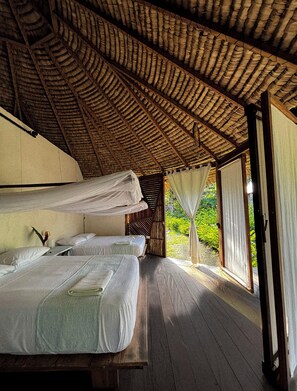 A room with two beds, a wooden floor, and a thatched roof. - Luzul Ecohotel (Arusi)