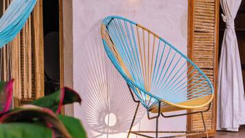 A hammock, a chair, and a wall-mounted light fixture in a room with a wooden floor and a white wall.