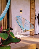 Una hamaca, una silla y un aplique en una habitación con piso de madera y pared blanca.