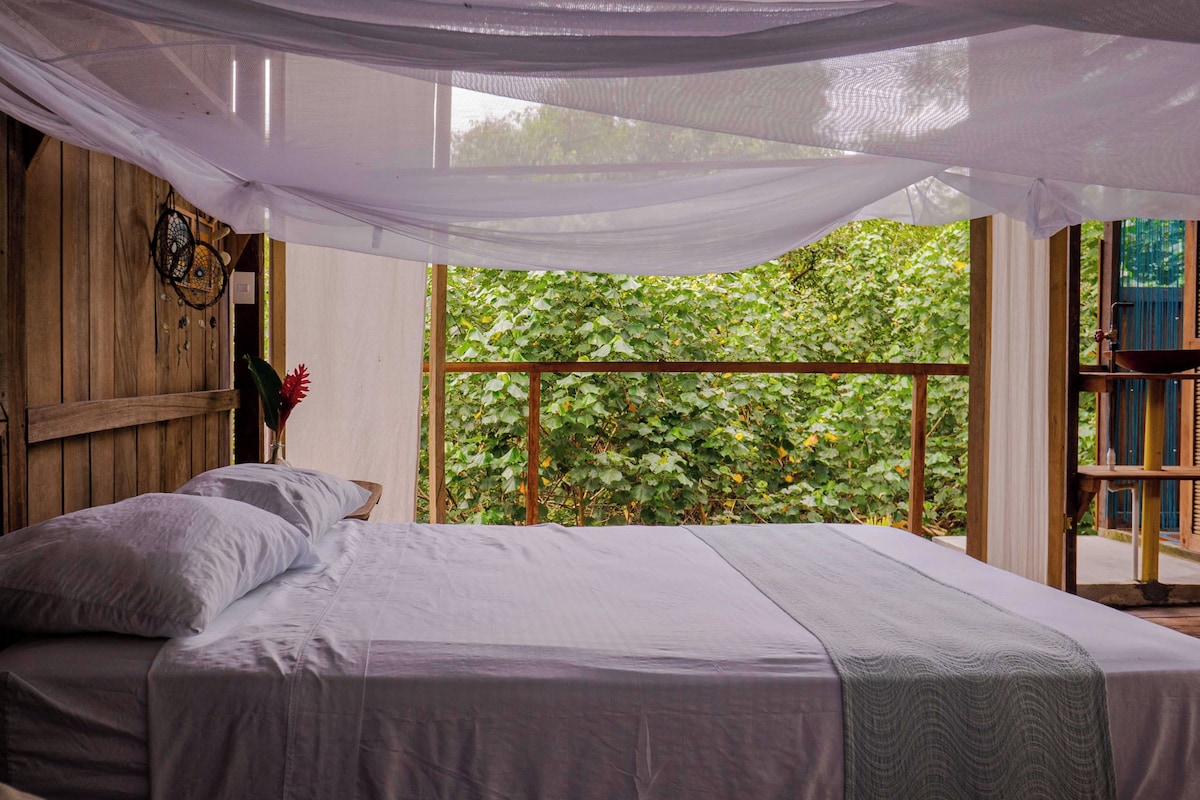 A bed with a canopy, a wooden wall, and a view of greenery outside.