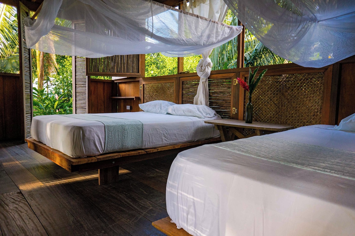 A room with two beds, a wooden floor, and a canopy bed with a mosquito net.