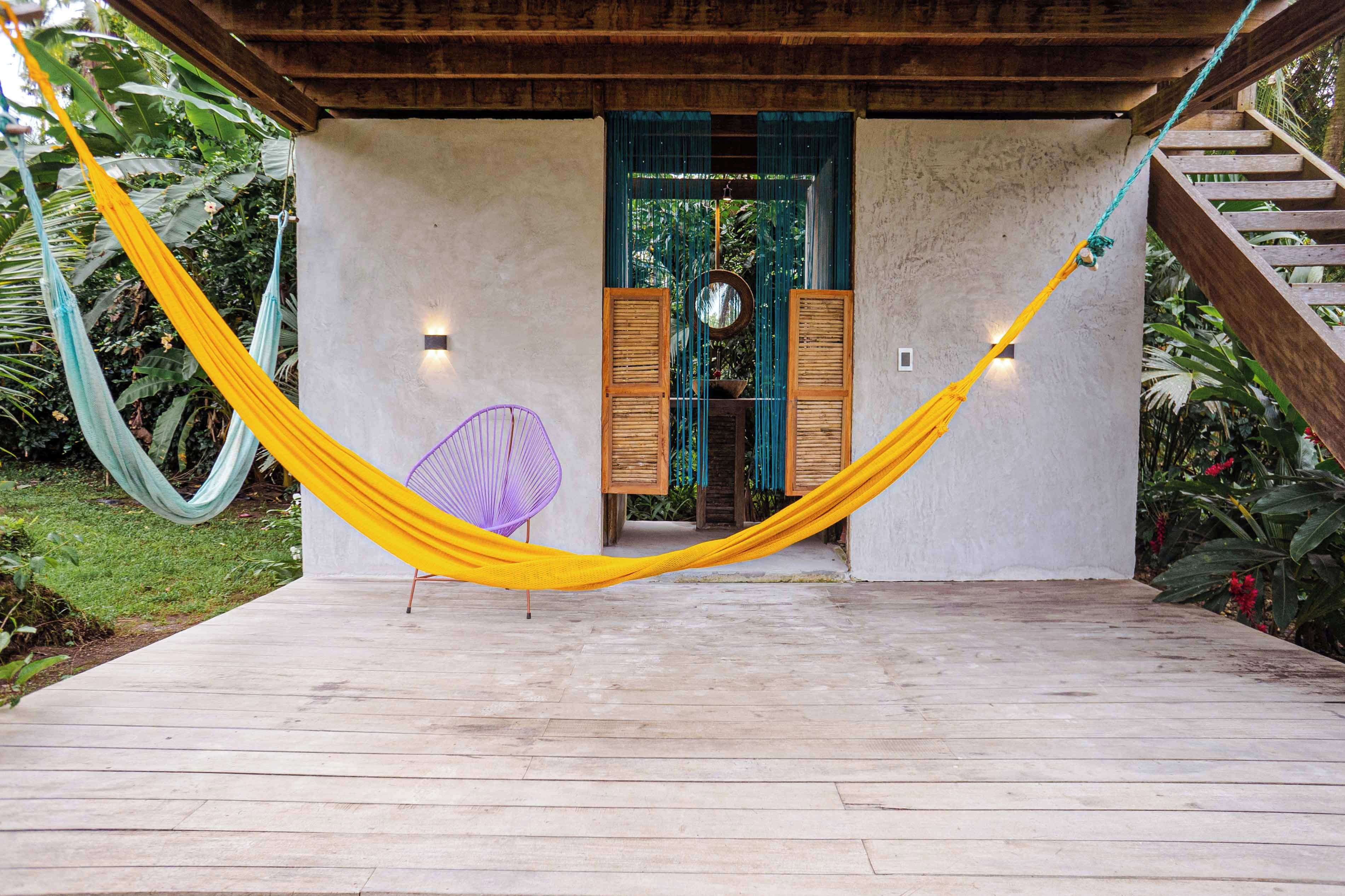A wooden deck leading to a building with a green door, a hammock, and a purple chair.