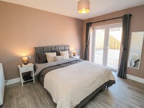 Ein Schlafzimmer mit einem Bett, Nachttischlampen, einem Nachttisch und Blick durch eine Schiebetür.