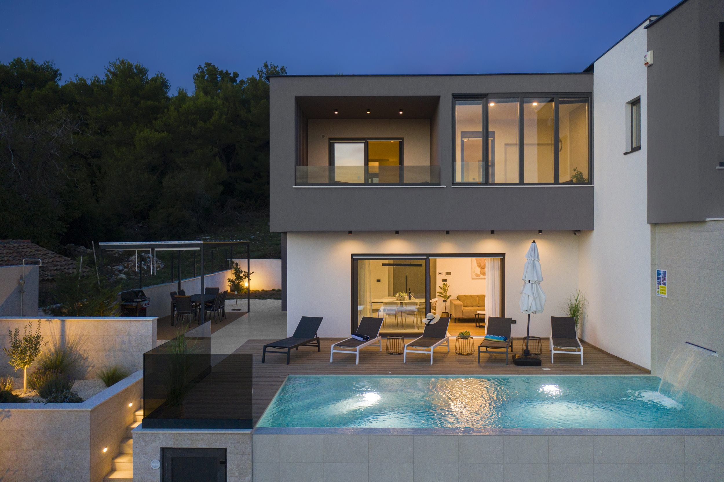 A modern two-story house with a swimming pool, outdoor seating, and a dining area.