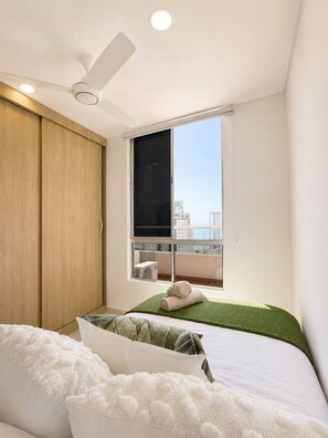 A bedroom with a bed, a ceiling fan, a window with a view of buildings, and a wooden wardrobe. - Sienna Grove | Terrace, Caribbean Views & Pool (Cartagena)