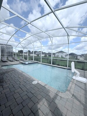 A covered outdoor swimming pool with lounge chairs and a hot tub, surrounded by a metal fence. - 🌴 Luxury Champions Gate Retreat 9 Bedrooms Pool, Game Room, Themed Fun & Resort (Davenport)
