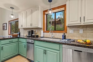 Een moderne keuken met groene kastjes, een RVS vaatwasser en een raam met uitzicht op de omgeving.