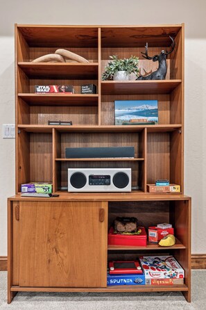 Ein Holzregal mit verschiedenen Gesellschaftsspielen, einem Radio und Dekorationselementen.