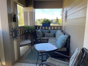 A covered outdoor seating area with a table and chairs, a wicker sofa with cushions, a potted plant, and a decorative wall piece. - SunDance Film Festival Travelers: Cosy 2-bedroom condo  in adorable Broomfield (Broomfield)
