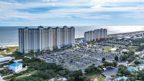 A high-rise hotel with multiple floors, a parking lot, and a view of the ocean. - Beachfront Resort Condo with Pools, Spa, Club House and Pickleball Court (Gulf Shores)