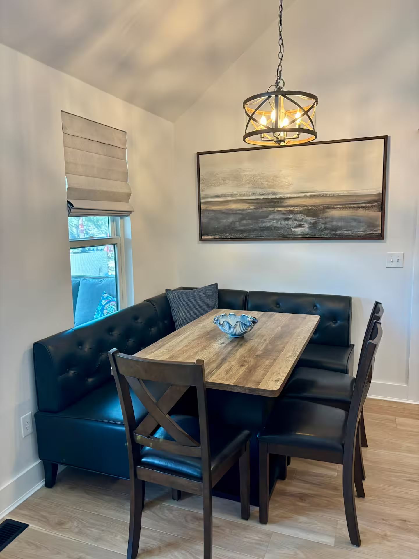 Un comedor con mesa de madera, asientos de cuero oscuro, una lámpara colgante y un cuadro en la pared.