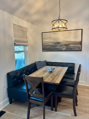 A dining area with a wooden table, dark leather seating, a pendant light, and a painting on the wall.