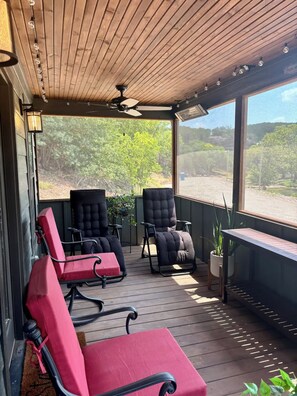 Un espace extérieur abrité, aménagé avec deux chaises noires et une chaise rouge, un ventilateur de plafond et une vue sur un paysage naturel.