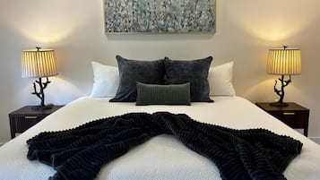 A neatly made bed with a black and white patterned blanket, two bedside lamps, and a painting above the bed.