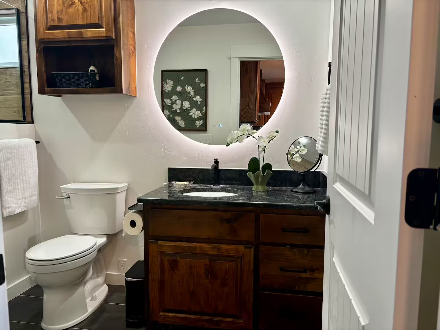 Un baño con inodoro, lavamanos, espejo y armarios de madera.