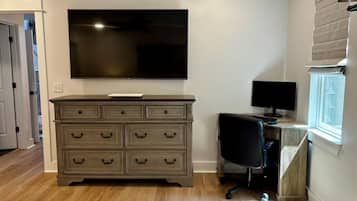 Een slaapkamer met een bed, een dressoir, een televisie, een bureau met een computer en een raam.